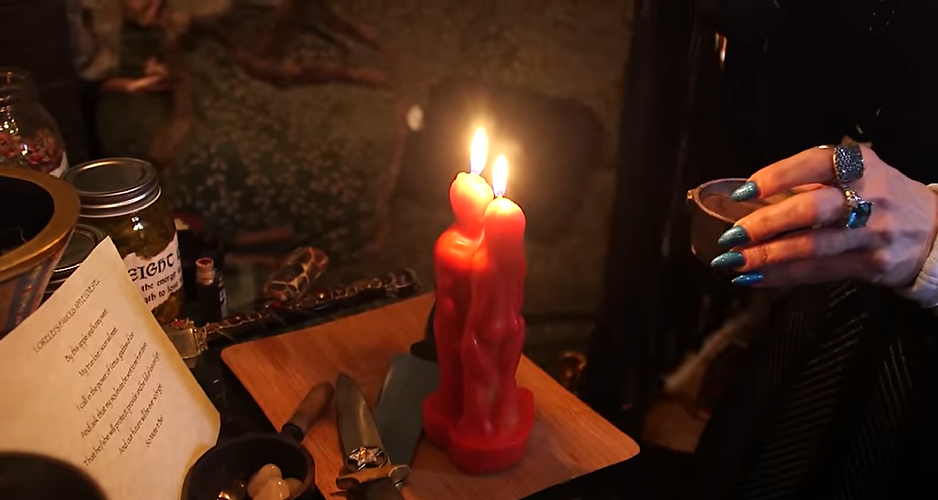Person holding a red candle with another candle in the background on a wooden surface.